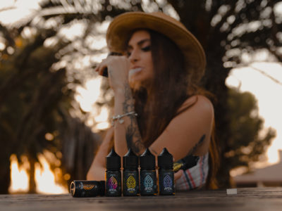 woman vaping cbd in nature sitting on a table with cbd vape juices