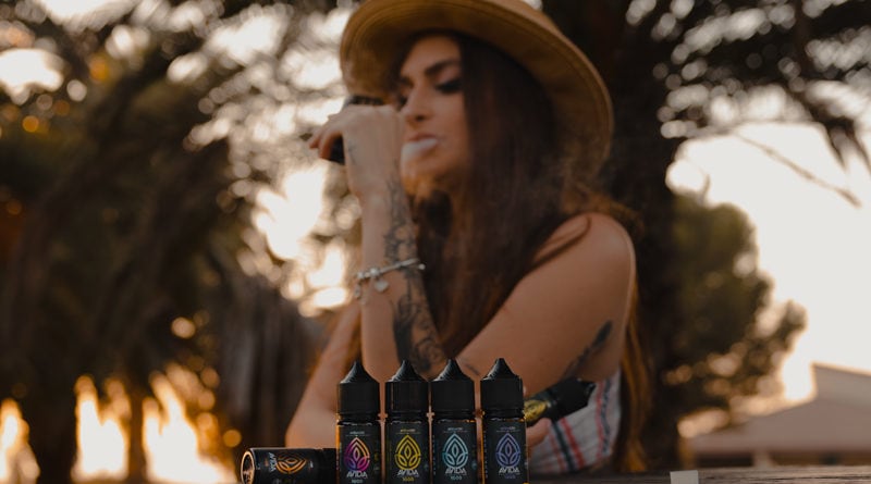 woman vaping cbd in nature sitting on a table with cbd vape juices