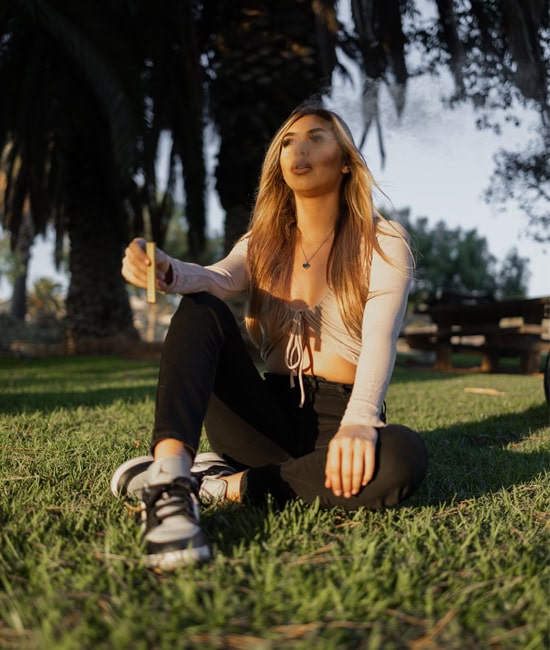 girl sitting on grass at the park vaping a mango cbd vape pen