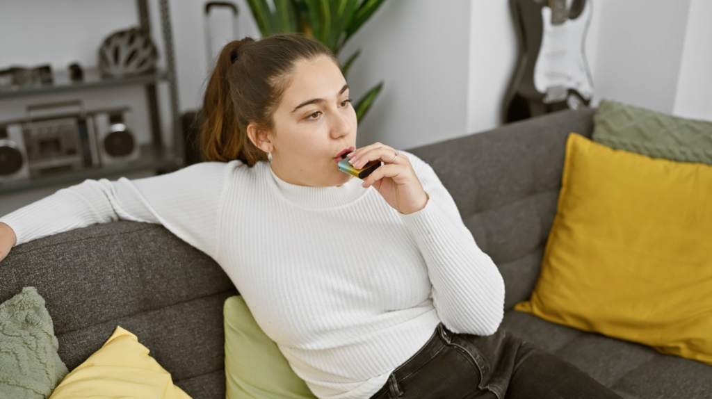 a woman sitting on grey couch relaxing and vaping 